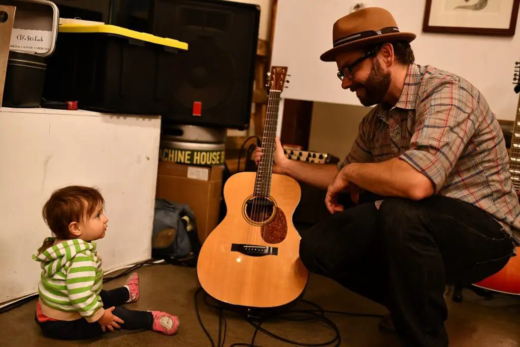 homme avec une guitare accroupi devant son enfant